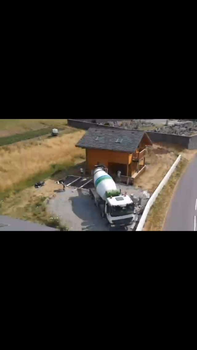 Aerial view of a concrete mixer truck parked beside a timber-clad building during a foundation pour on a construction site.
