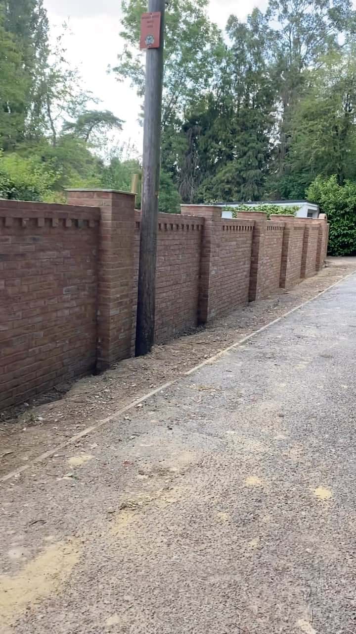 Finished red brick boundary wall with decorative dentil course and square piers alongside a gravel driveway.