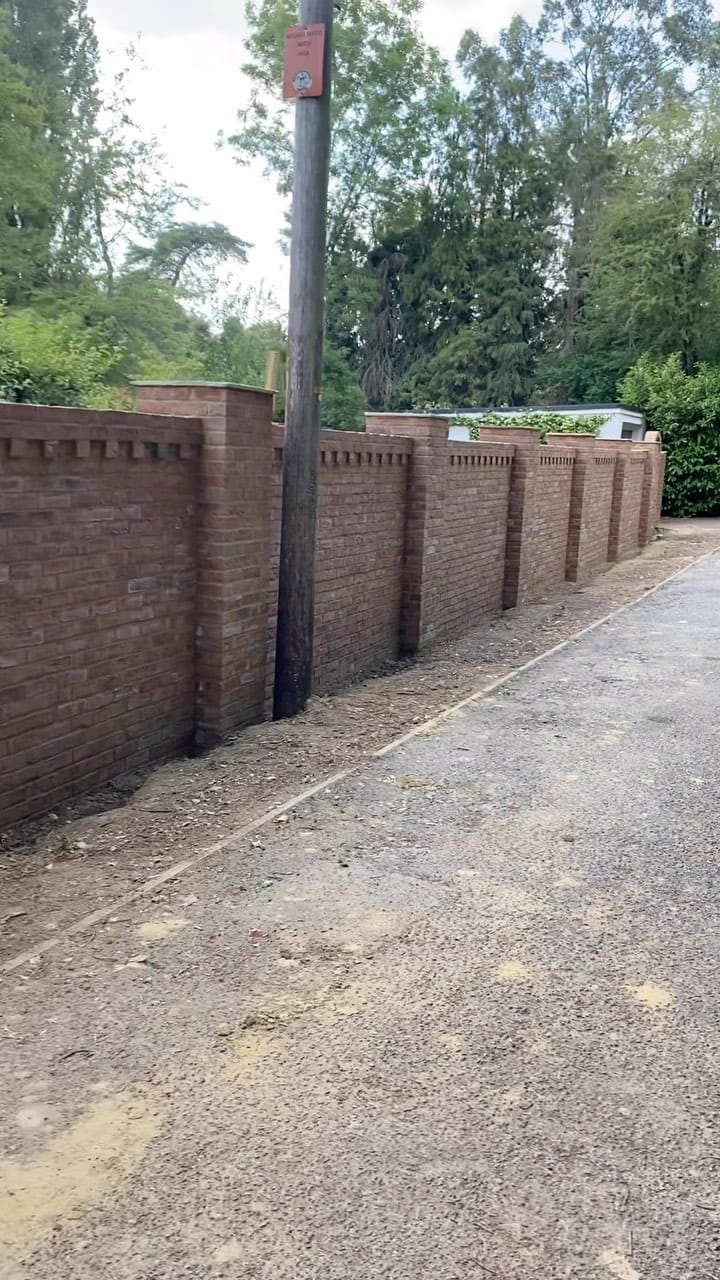 New brick boundary wall with decorative pillars along a driveway