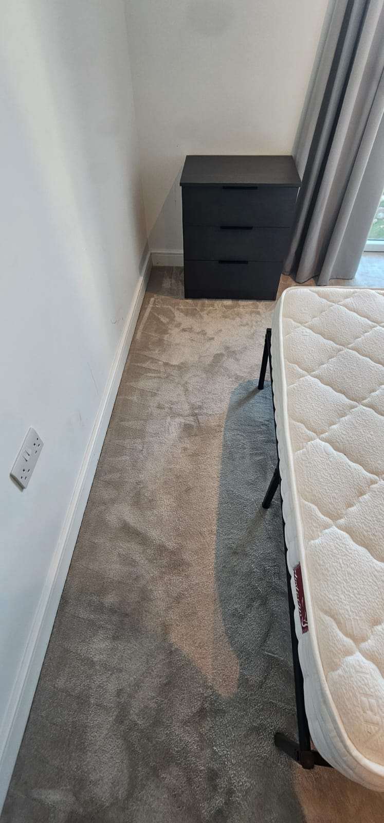 Cleaned beige bedroom carpet with vacuum marks beside black drawers and a mattress