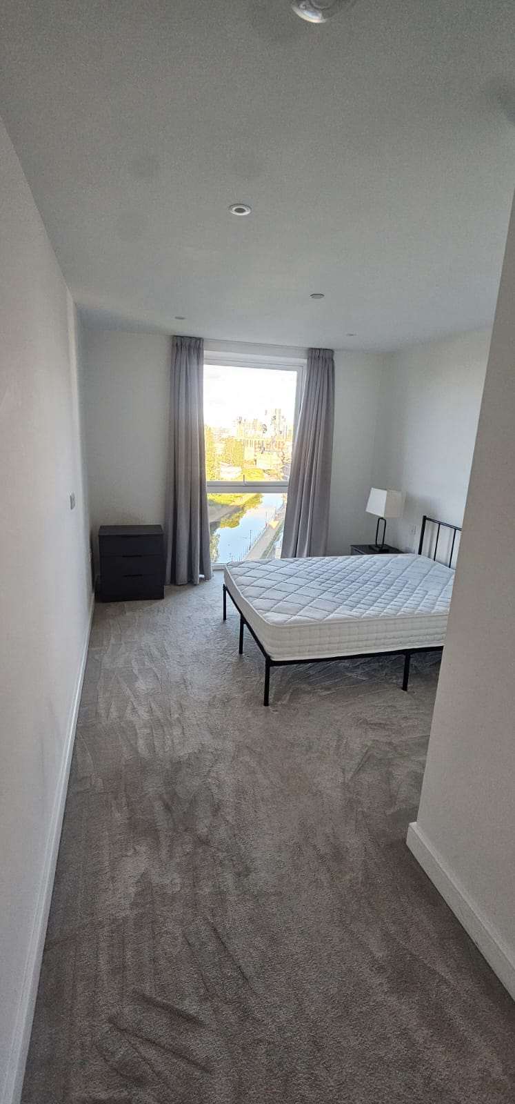 Empty bedroom with a bed frame and large window and a freshly cleaned grey carpet