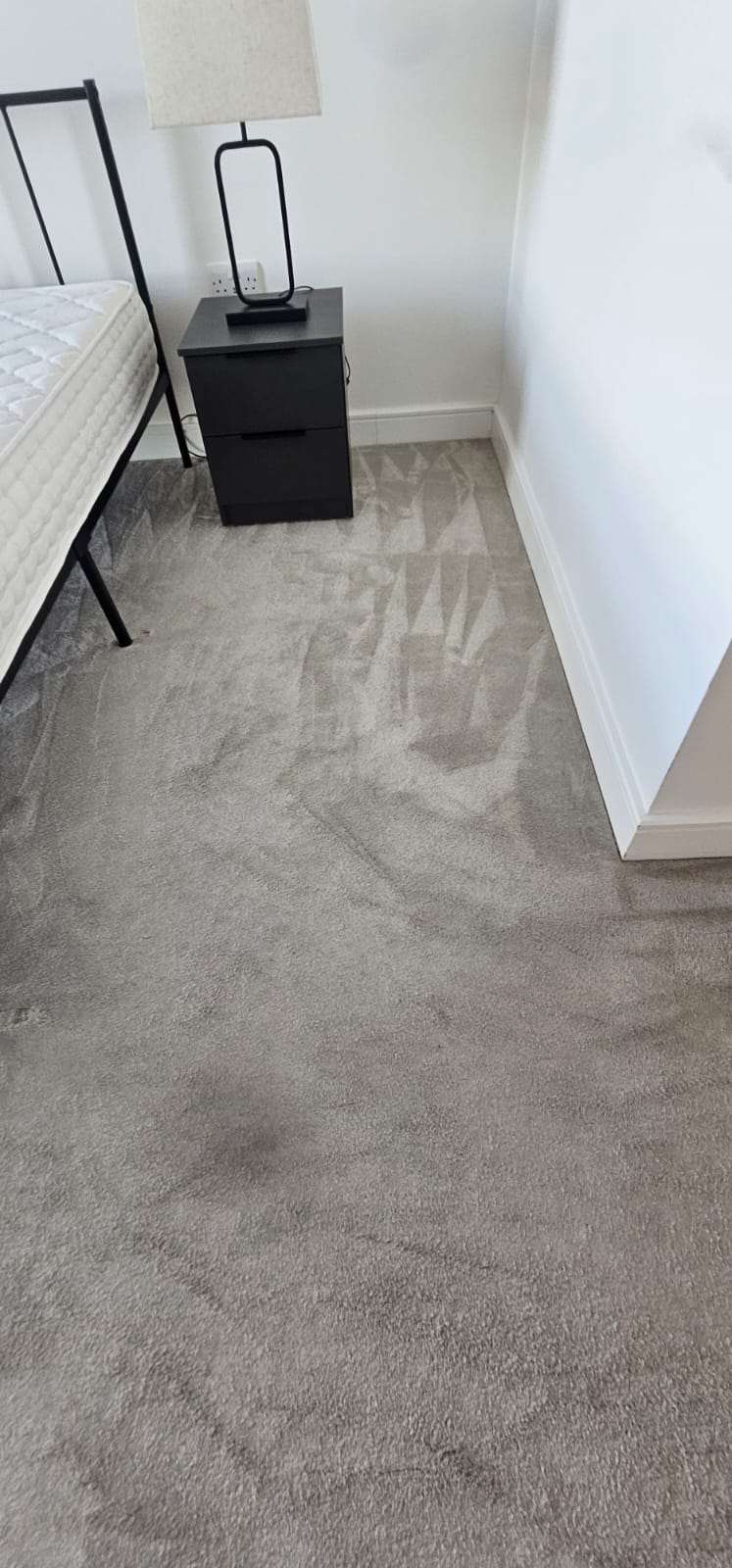 Close-up of a freshly cleaned grey bedroom carpet with vacuum lines beside a black bedside table