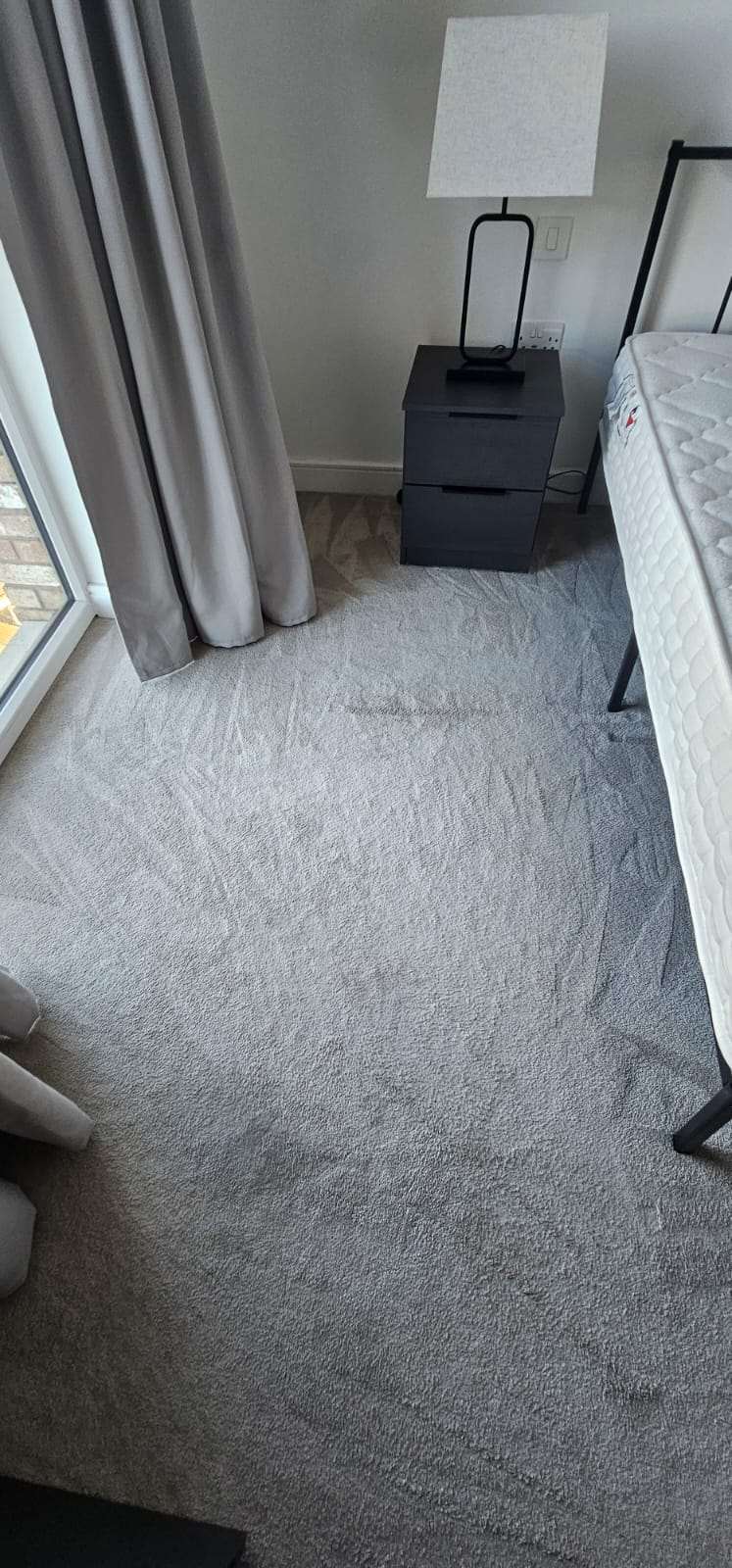 Freshly cleaned grey bedroom carpet with vacuum lines beside a bedside table and mattress