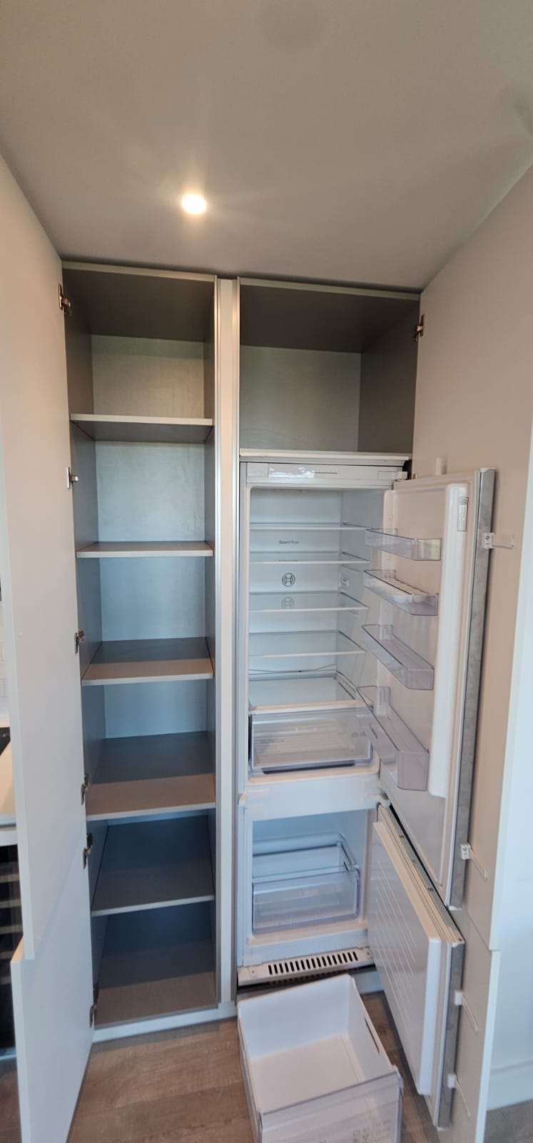 Empty clean larder cupboard beside an empty integrated fridge