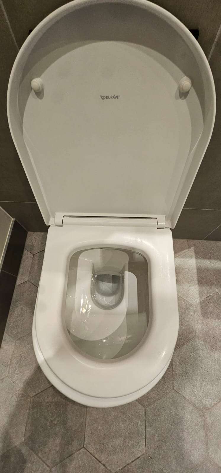 Clean white Duravit toilet with the lid raised in a grey tiled bathroom after cleaning