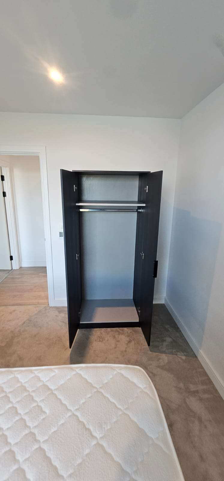 Empty bedroom with an open black wardrobe and bare mattress ready for a new tenant