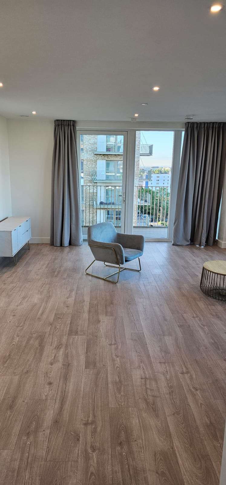 Empty, freshly cleaned flat lounge with wood flooring and a single armchair.