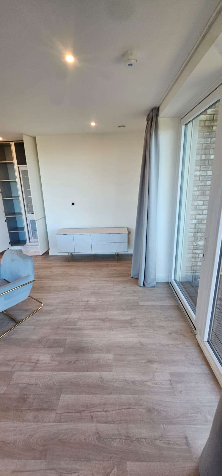 Empty, freshly cleaned flat lounge with a sideboard and balcony doors.