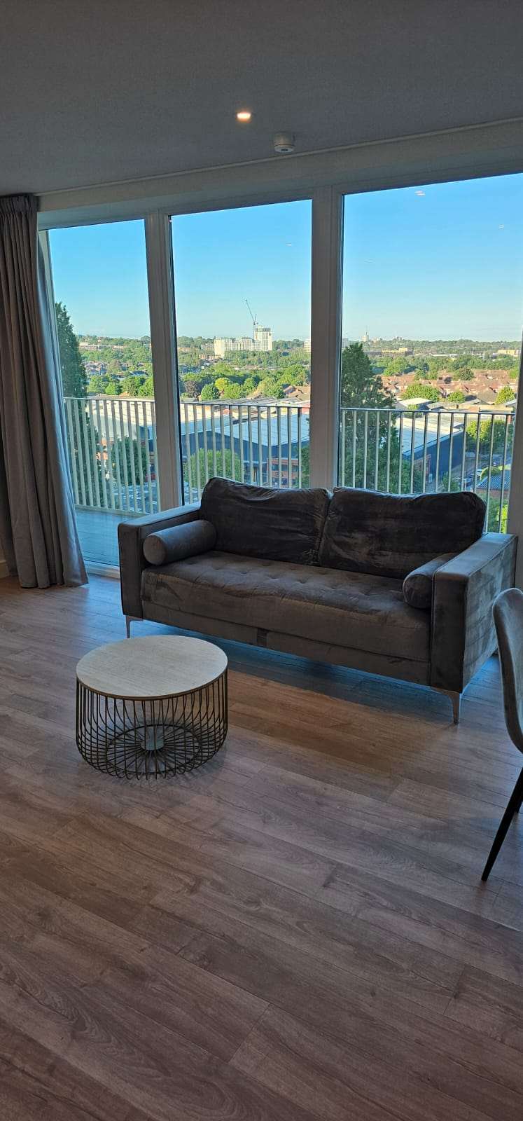 Clean modern living room with a velvet sofa and floor-to-ceiling windows overlooking the city.
