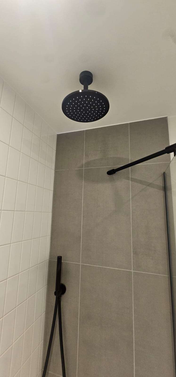 Black ceiling-mounted rainfall shower head in a grey and white tiled shower