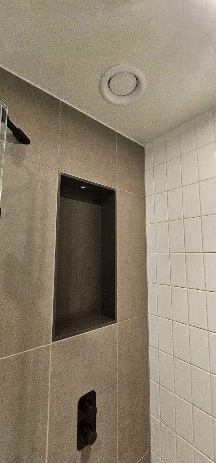 Recessed shower niche in a grey and white tiled wall with an extractor vent above
