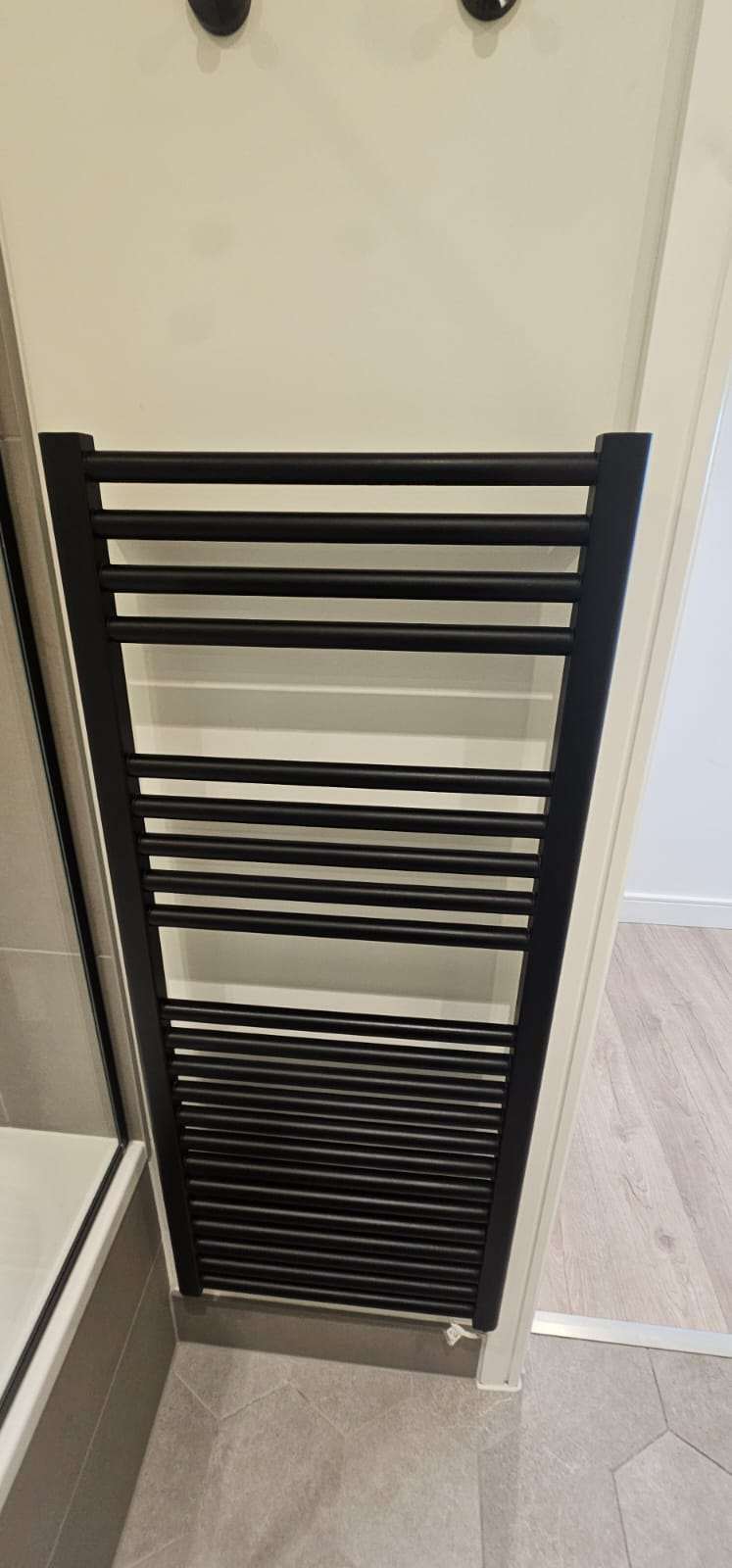 Black heated towel rail radiator mounted on a bathroom wall