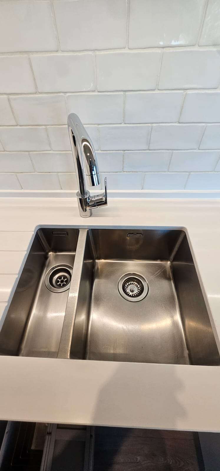 Polished stainless steel double kitchen sink with chrome mixer tap against white tiles