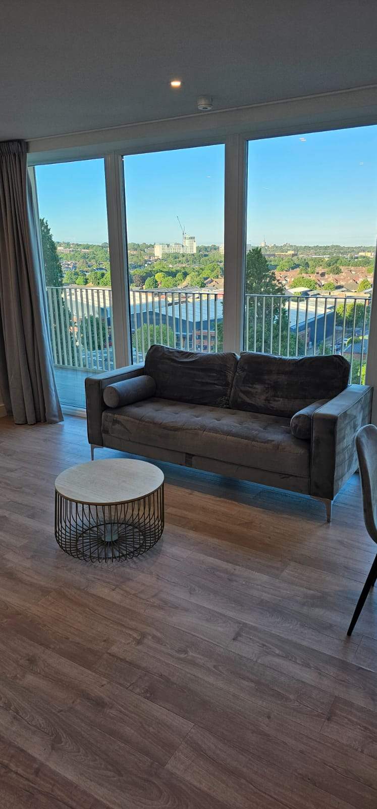 Clean modern living room with a velvet sofa and floor-to-ceiling windows overlooking the city.