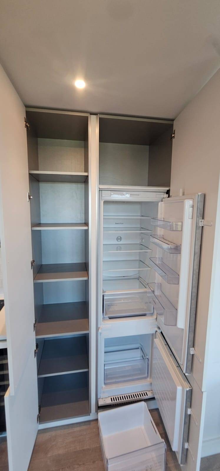 Empty clean larder cupboard beside an empty integrated fridge