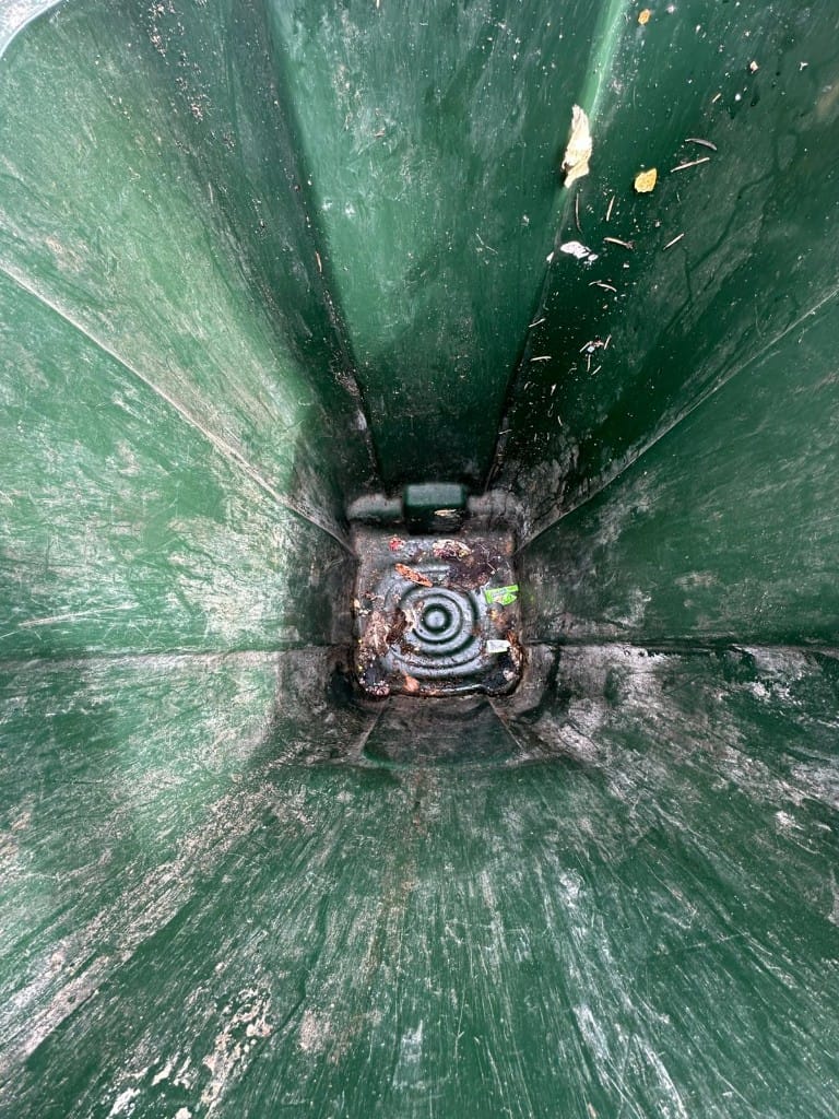 Dirty interior of a green wheelie bin with grime, food residue, and leaf debris before cleaning