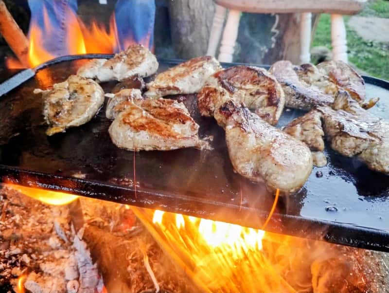 Game meat cooking on a plancha over an open fire