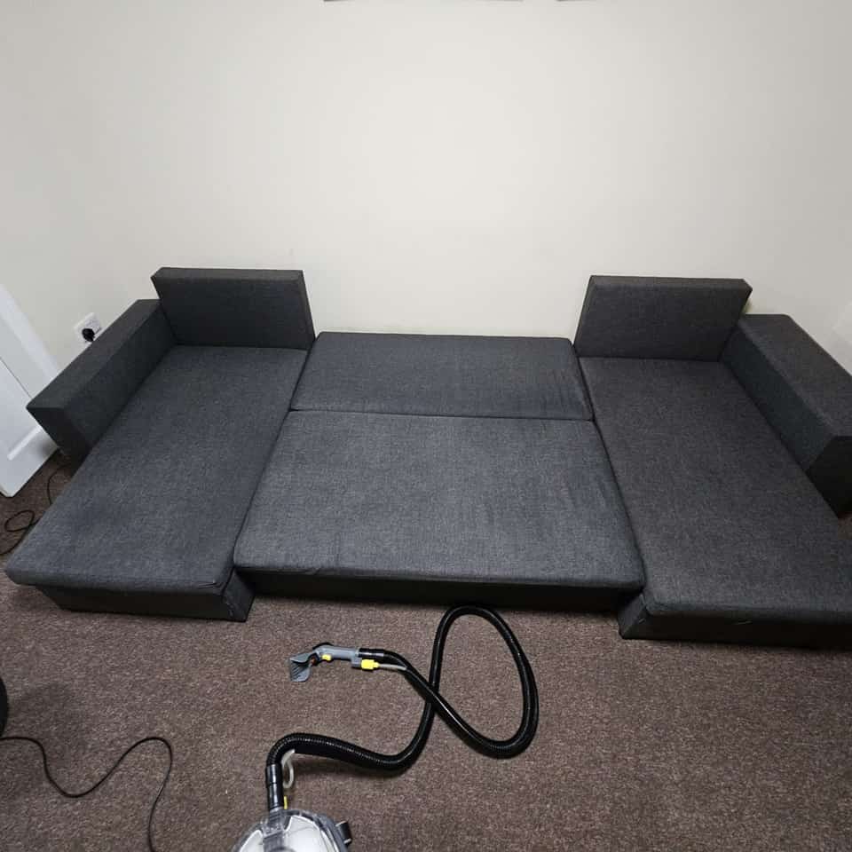 Clean grey corner sofa bed after upholstery cleaning with the extractor on the floor.