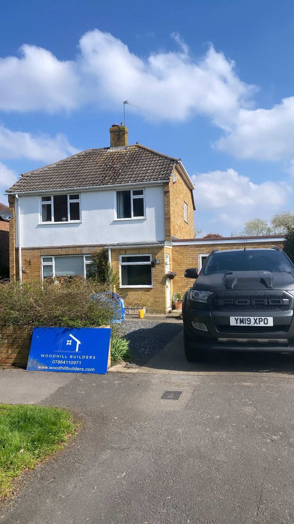 Woodhill Builders site sign in front of a two-storey house with a black Ford Ranger parked on the driveway.