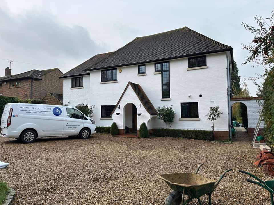 Renovated white brick house with black windows and a branded Woodhill Builders van on the gravel driveway