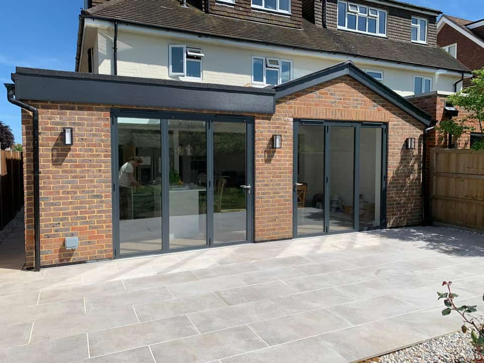 Finished red brick rear extension with dark grey bi-fold doors opening onto a large light porcelain patio.
