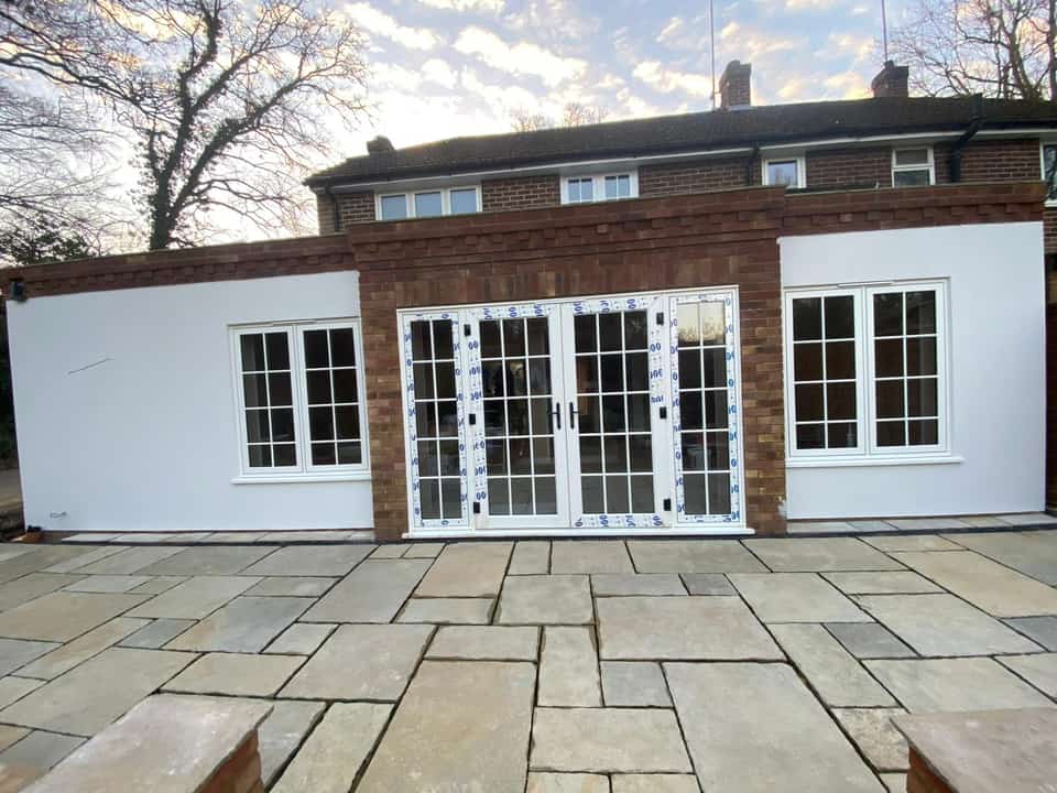 Finished single-storey rear extension with brick centre bay, rendered wings, French doors, and large stone patio.