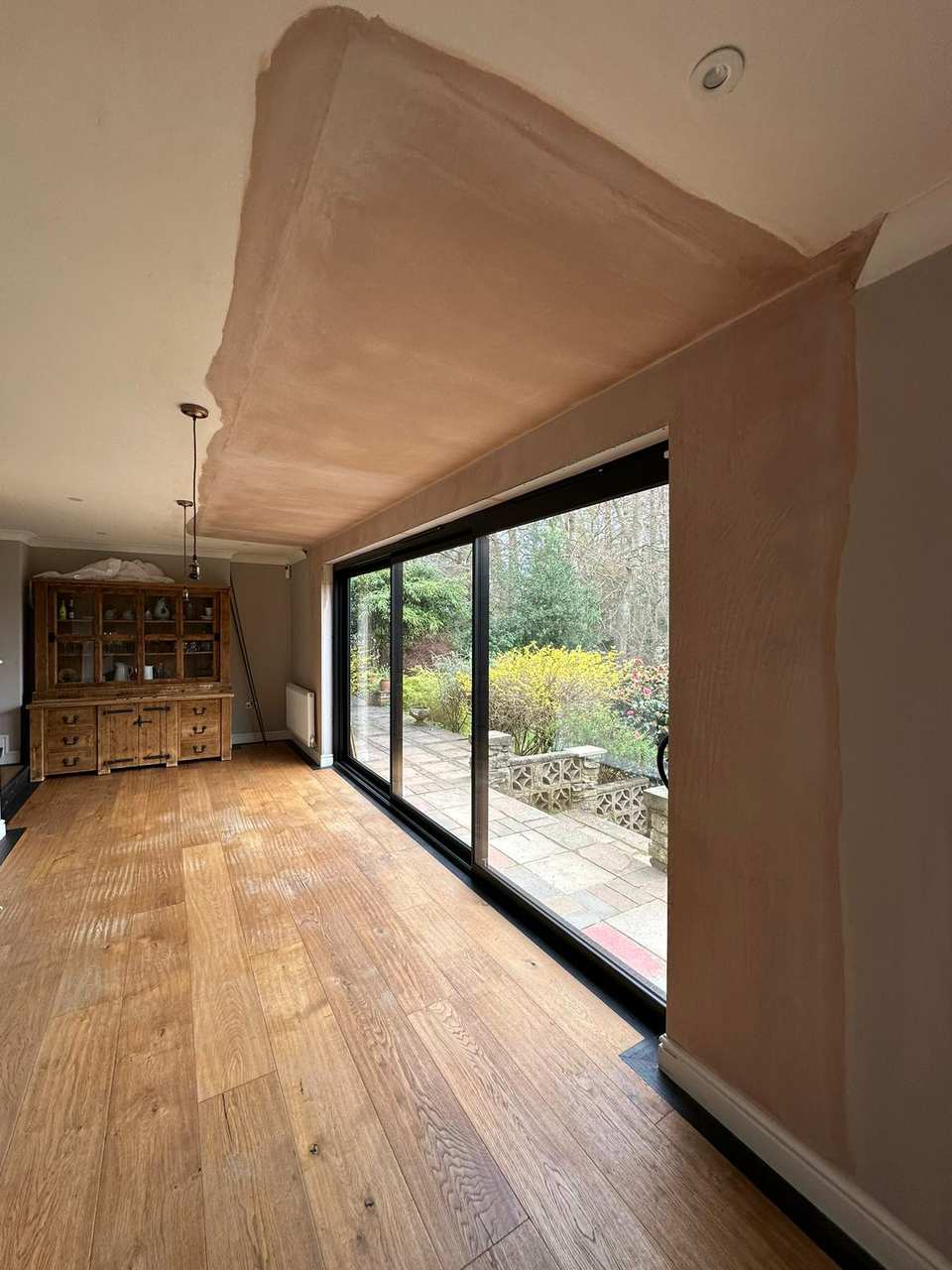 Interior room with fresh plaster around new black-framed sliding glass doors overlooking a garden patio