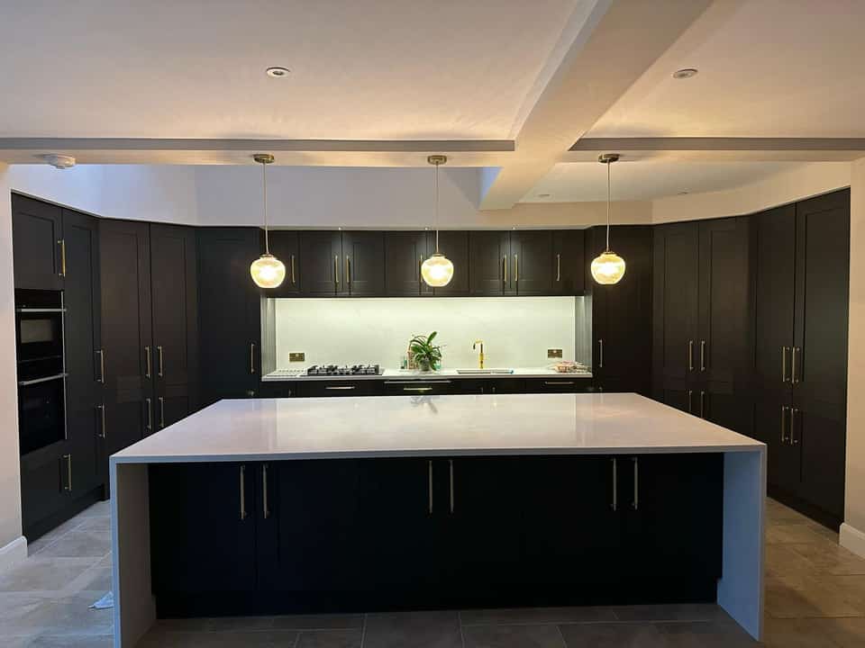 Finished modern navy kitchen with white marble waterfall island and gold pendant lights.