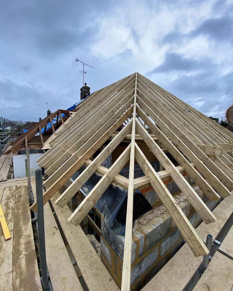 Close-up of timber roof rafters forming a multi-pitched loft conversion frame viewed from scaffolding.