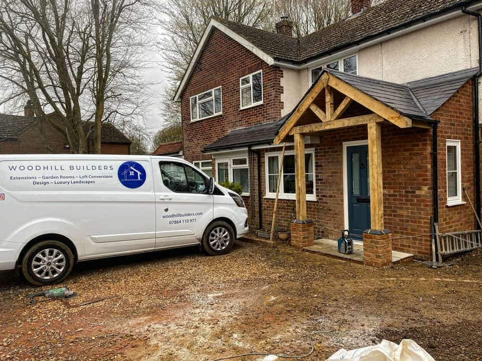 Woodhill Builders branded van parked in front of a completed oak-framed brick porch with a dark blue front door.