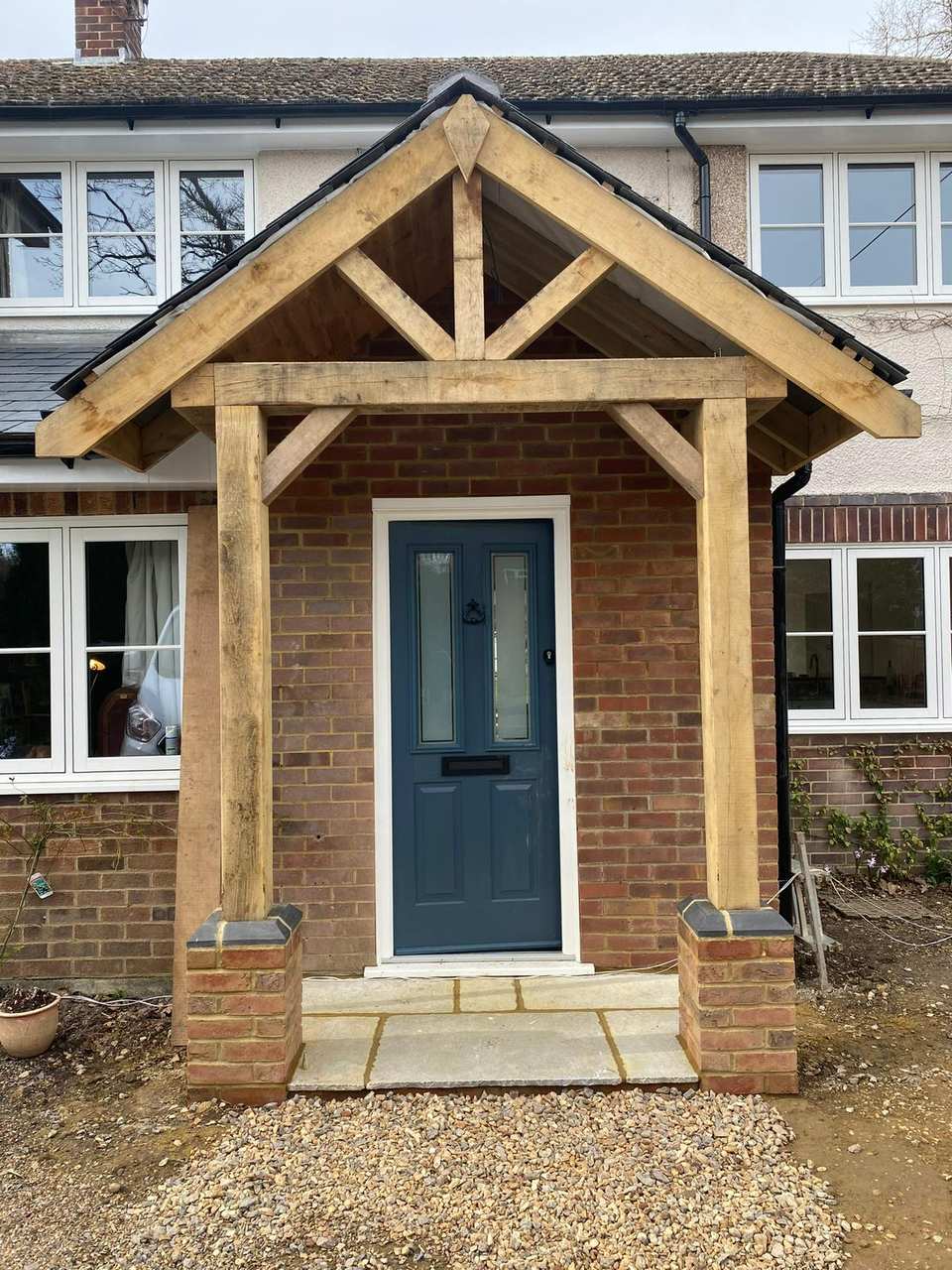 New oak timber porch with king-post truss, brick plinths, and a dark blue front door.