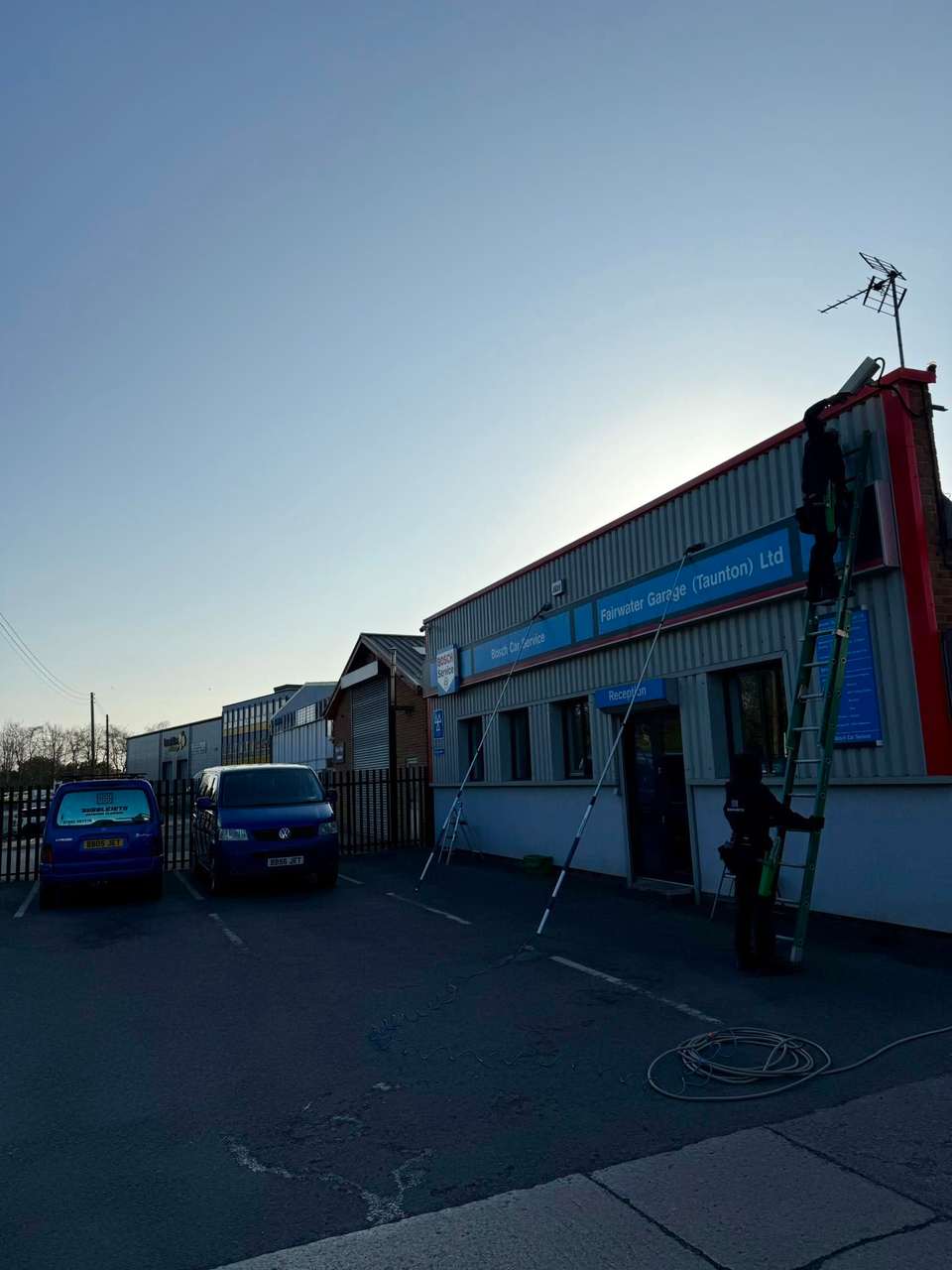 Cleaner using a reach pole to work at gutter height on a building at dusk