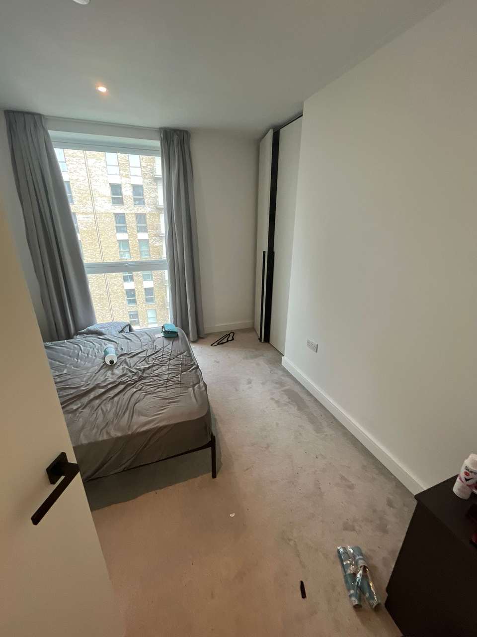 Tidy bedroom with a made bed and cleaning bottles beside a large window after clearing