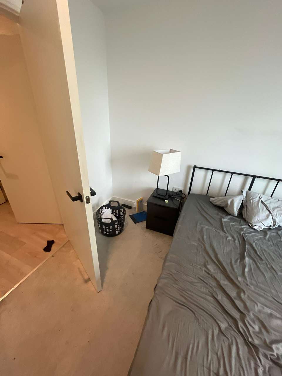 Tidy bedroom with a made bed, bedside lamp and laundry basket after clearing