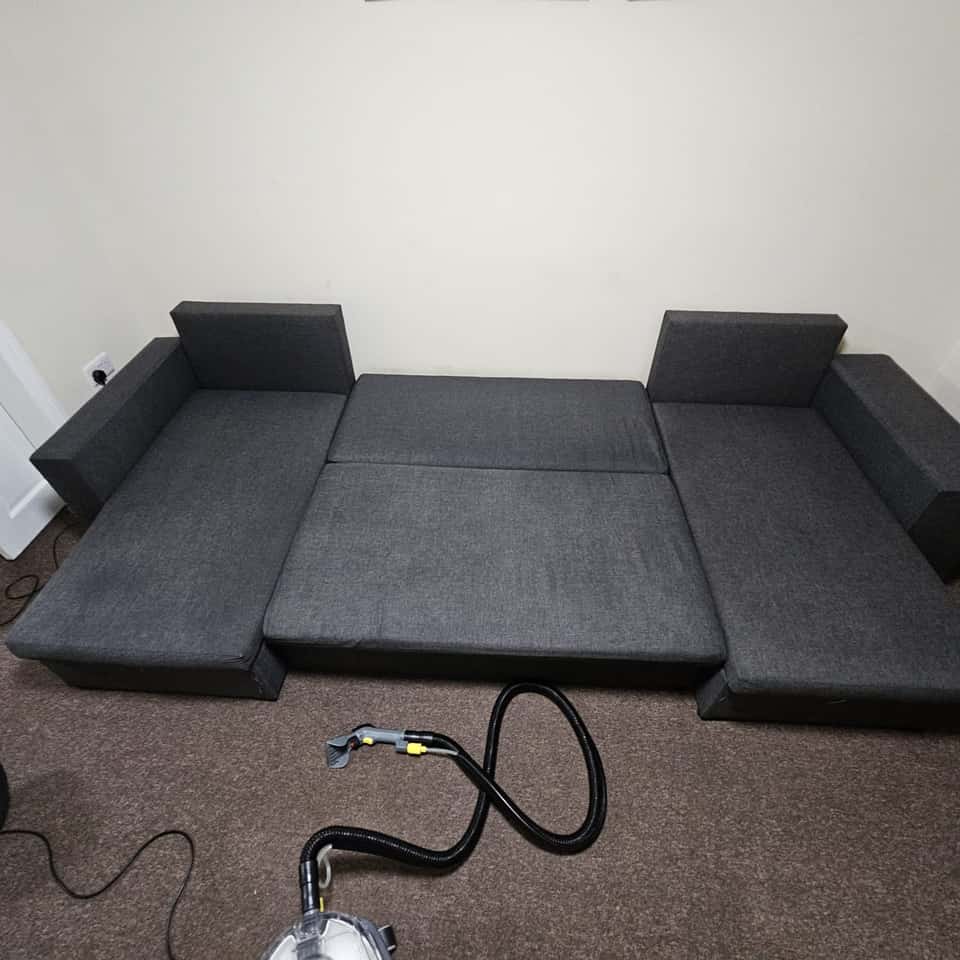 Clean grey corner sofa bed after upholstery cleaning with the extractor on the floor.