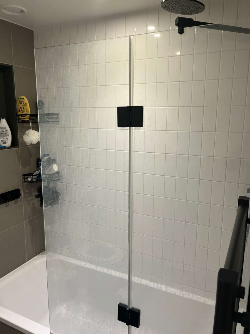 Clean white-tiled shower over bath with a spotless glass screen after cleaning