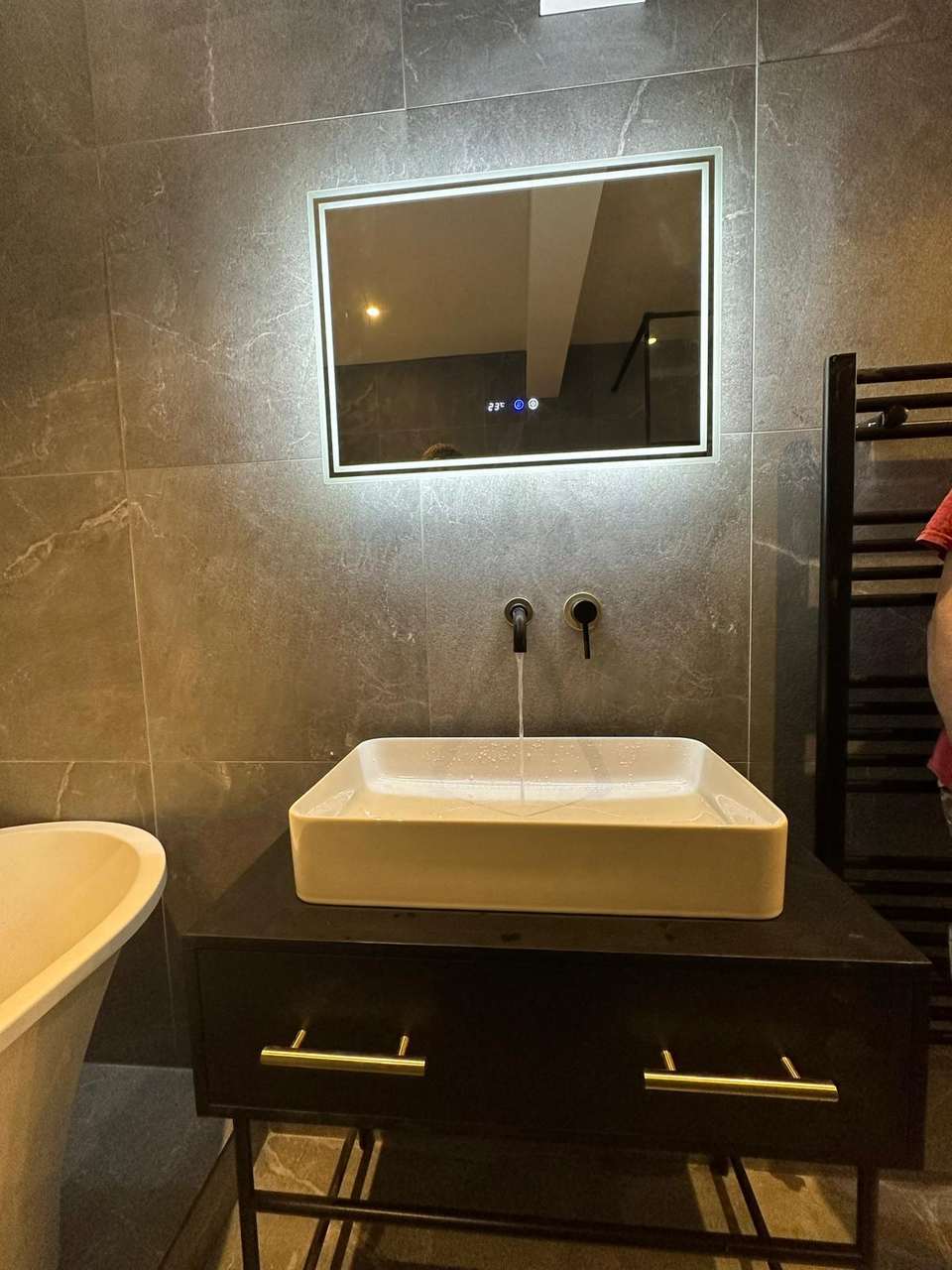 A modern bathroom with a dark floating vanity, vessel sink, LED mirror, and grey stone-effect wall tiles.