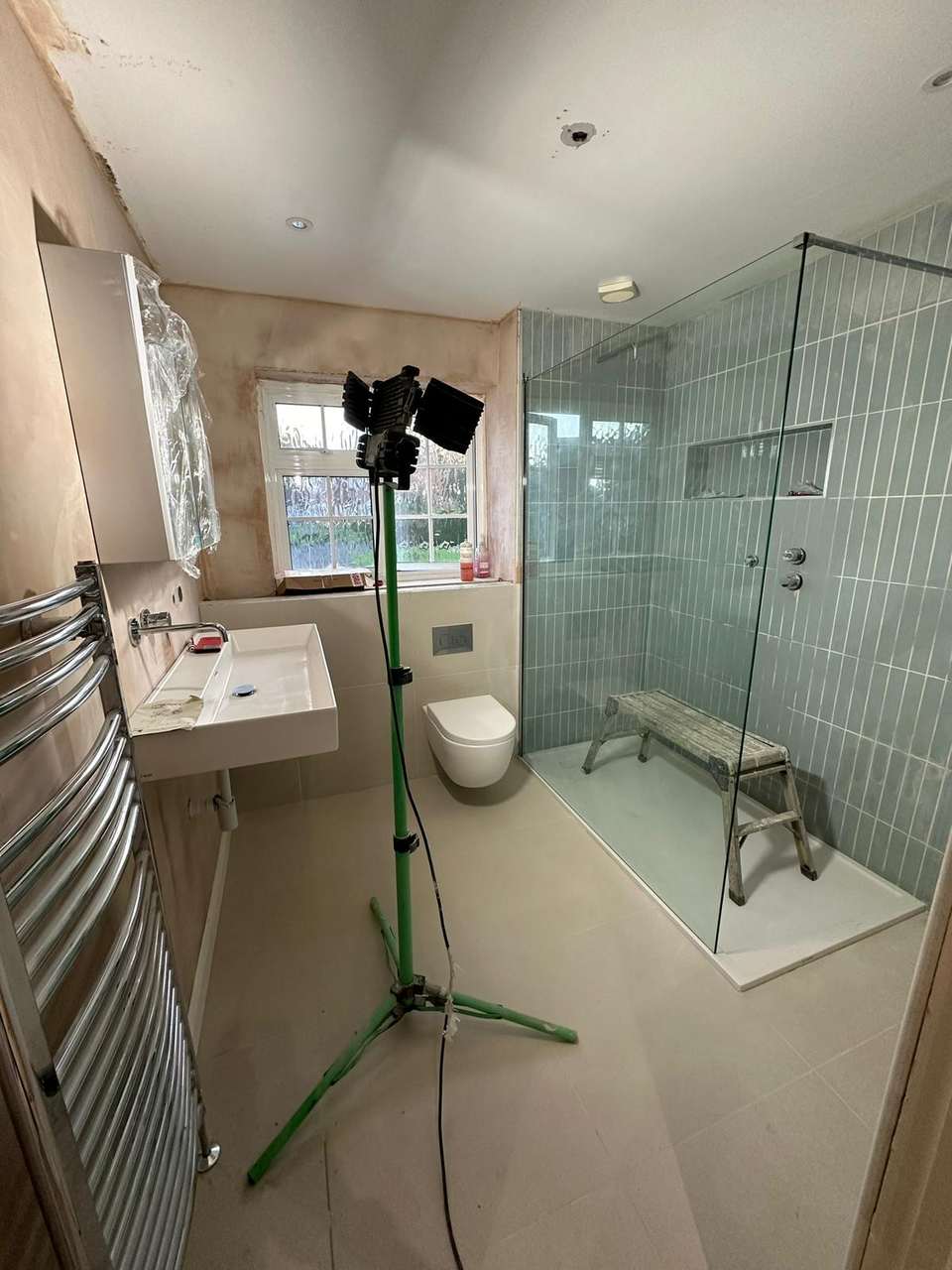 Modern bathroom under construction with glass walk-in shower, vertical blue tiles, wall-hung toilet, and large sink.