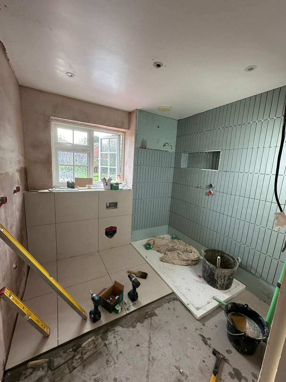 Bathroom renovation in progress with blue-grey wall tiles, shower tray, and plastered walls