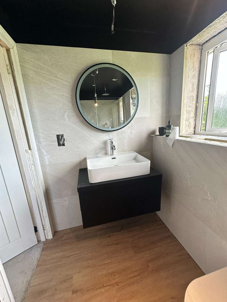 Modern bathroom with floating black vanity, vessel sink, and large circular backlit mirror.