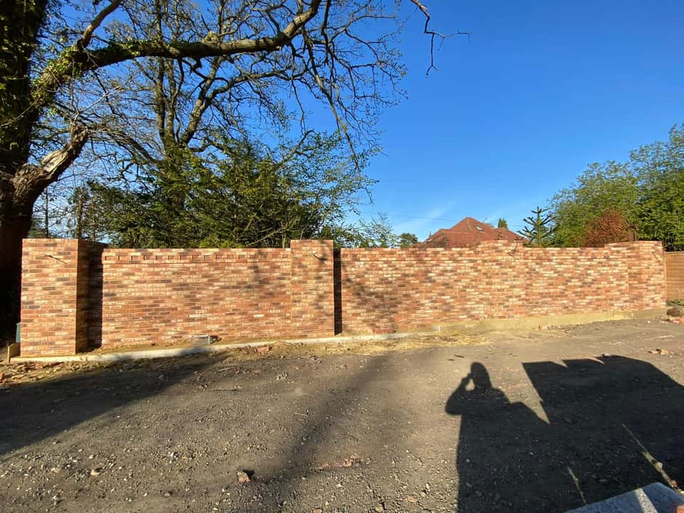 Completed multi-tonal brick boundary wall with square pillars and a decorative dogtooth course along the top.