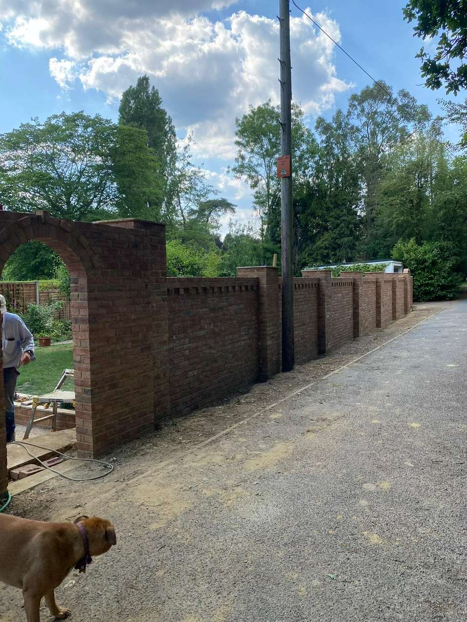 Long decorative red brick boundary wall with arched gateway and corbelled brick detailing