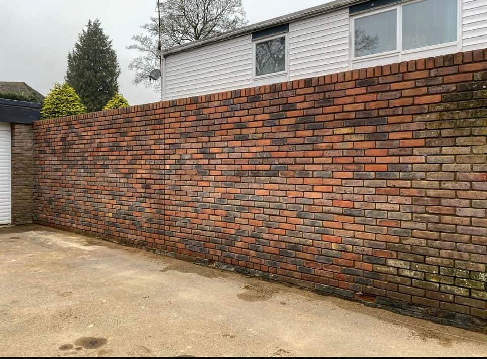 Finished multi-toned brick boundary wall with a vertical soldier-course top beside a weatherboard house