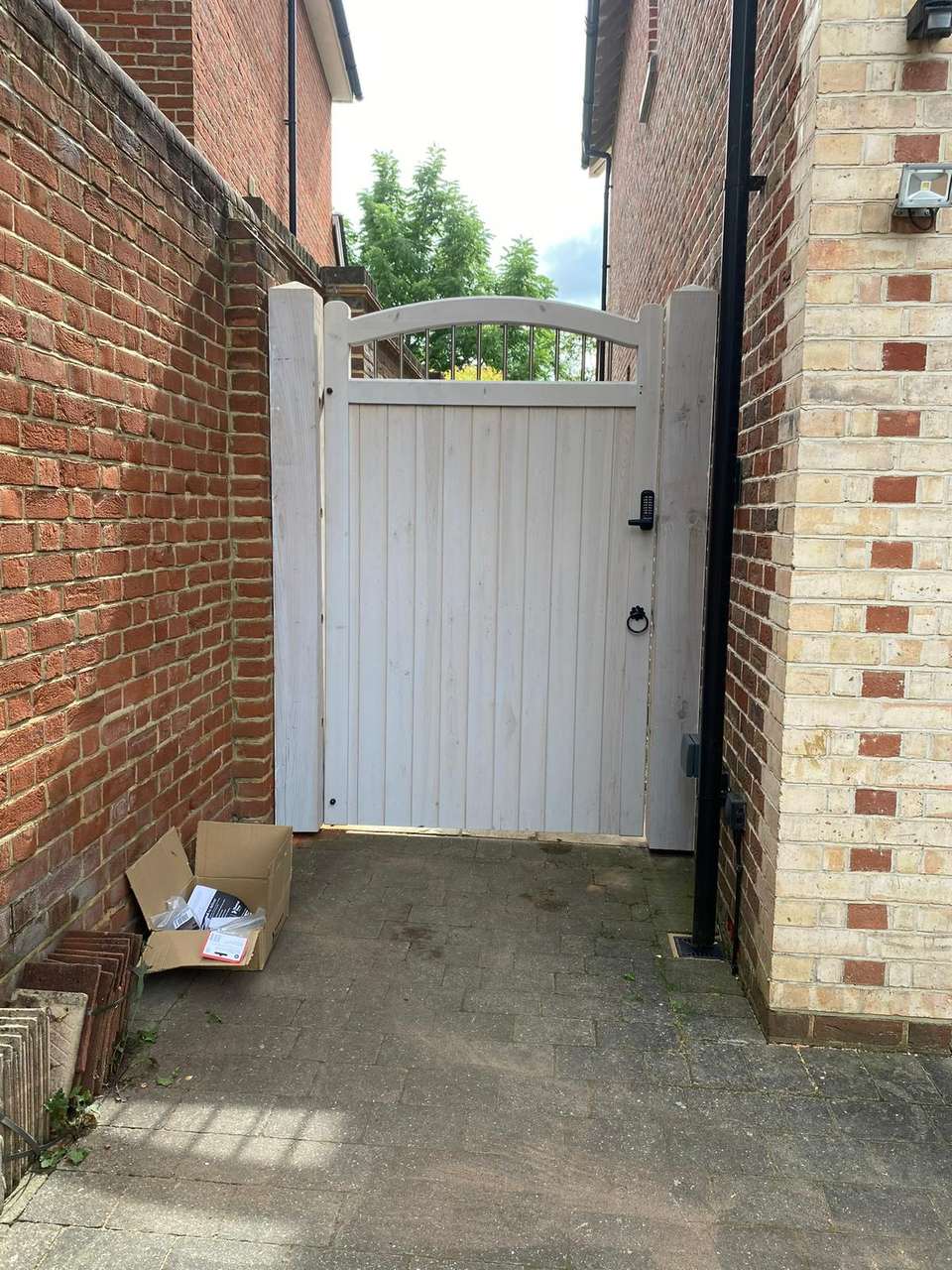 A newly installed light timber side gate with an arched top and digital keypad lock between brick walls.