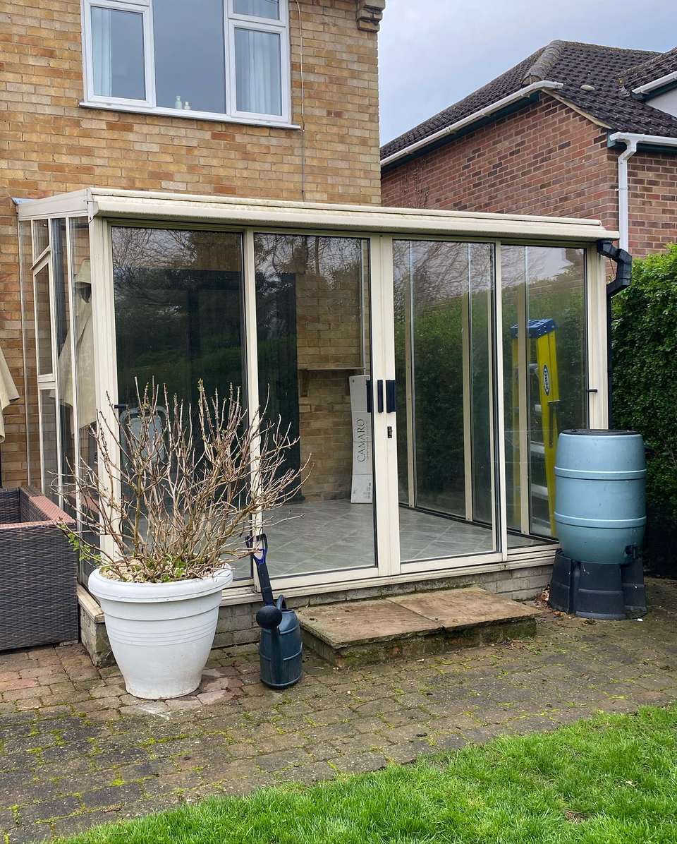 Glass-walled garden room extension with cream frames and sliding doors attached to a brick house above a paved patio.