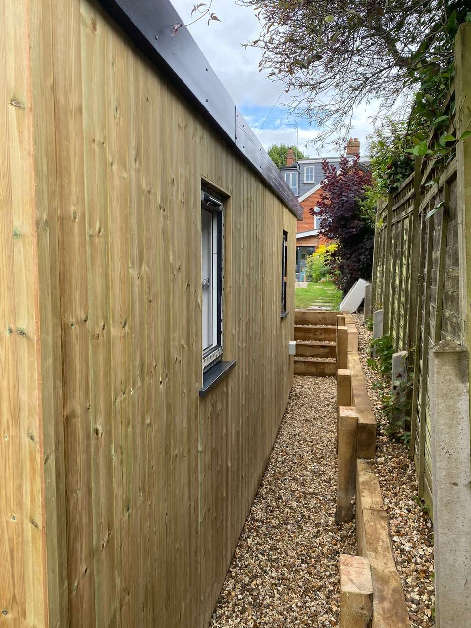 Side view of a finished timber-clad garden room with a gravel path and sleeper steps