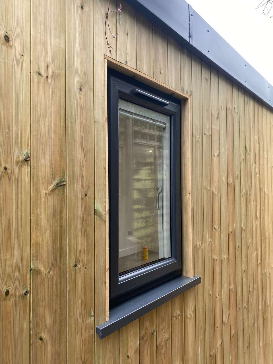 Anthracite grey window installed in vertical timber cladding on a garden room exterior.