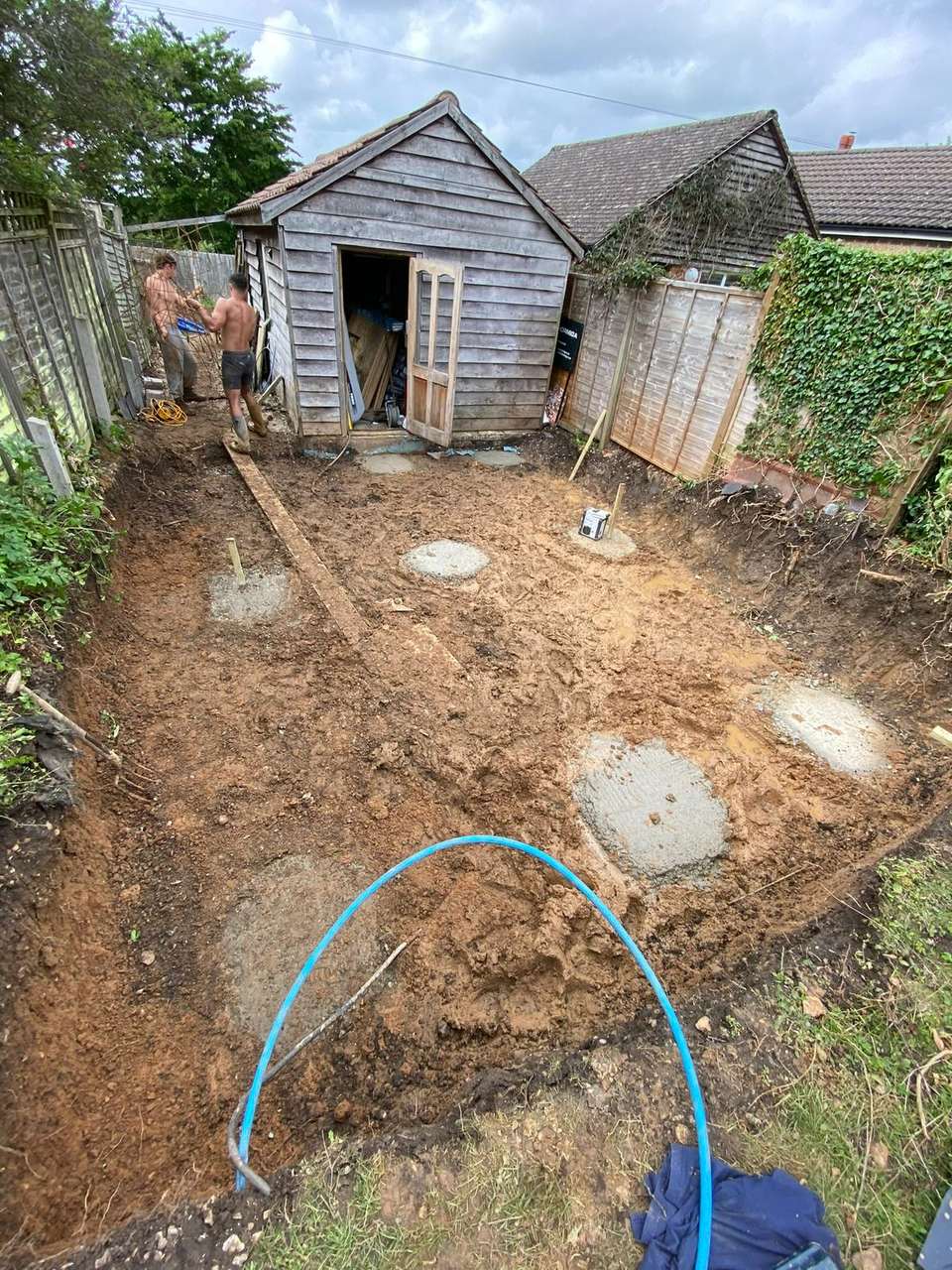 Excavated garden site with circular concrete pad foundations poured in the dirt.