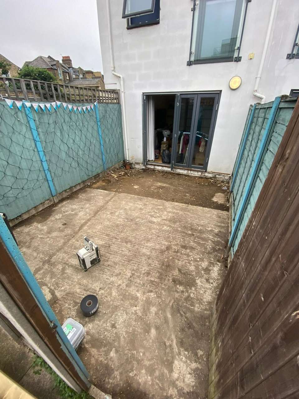 Freshly poured concrete slab filling a small fenced backyard beside bifold doors
