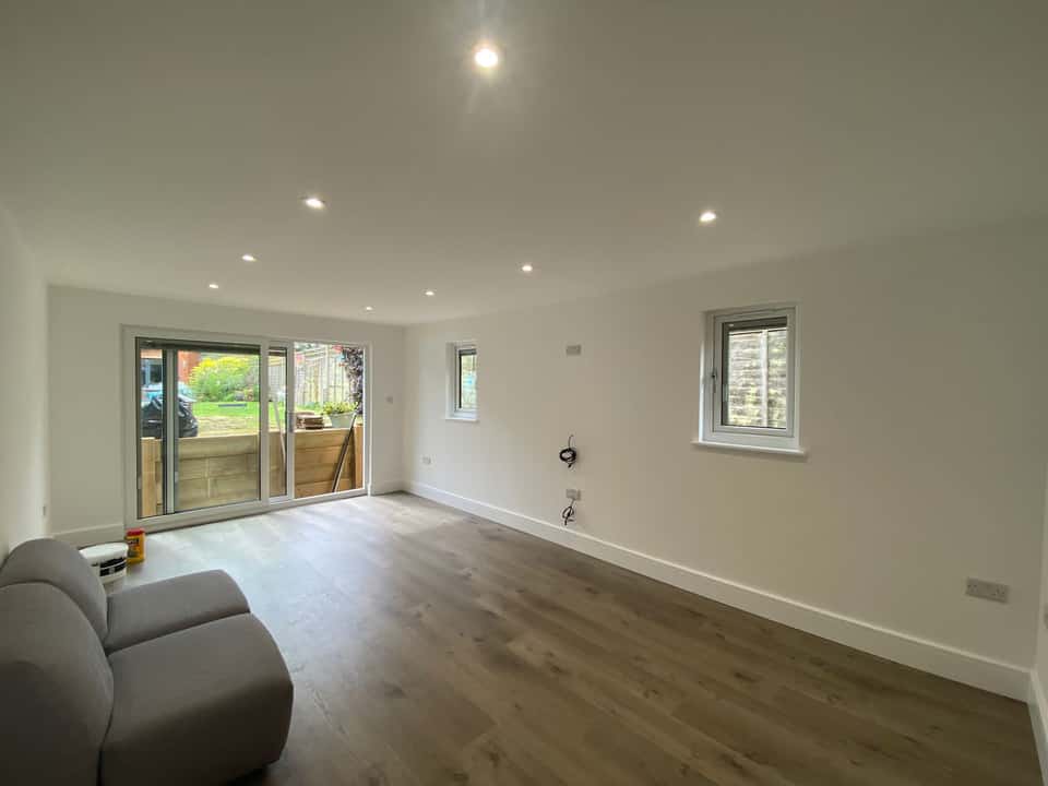 Bright newly finished extension living room with grey sliding doors, wood flooring, and recessed ceiling lights.